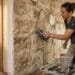 Artisan appliquant un enduit imitation pierre beige sur un mur avec une truelle