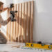 Artisan fixant des tasseaux verticaux en bois sur un mur blanc avec perceuse