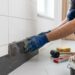Carreleur posant une plinthe en céramique contre un mur blanc avec truelle et colle à carrelage