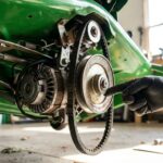 Mécanicien gantée inspectant le mécanisme d'embrayage de lame sous un tracteur tondeuse vert
