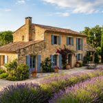 Quelles sont les couleurs idéales pour les volets d’une maison provençale ? Maison provençale en pierre ocre avec volets bleu-gris et lavande en premier plan