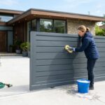 Propriétaire nettoyant un portail en aluminium gris anthracite avec une éponge douce et de l'eau savonneuse
