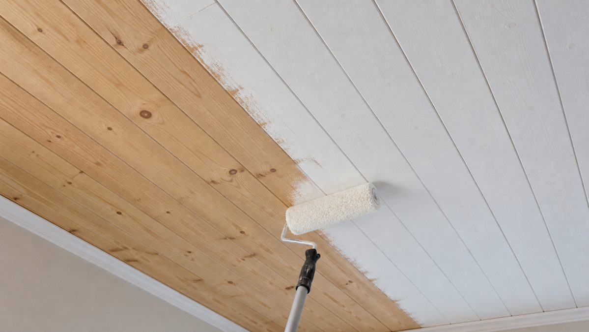 Application de peinture sur un lambris de plafond Rouleau de peinture blanche appliqué sur un plafond en lambris de bois