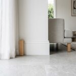 Plinthe en bois peinte en blanc sur un sol carrelé gris clair dans un salon lumineux