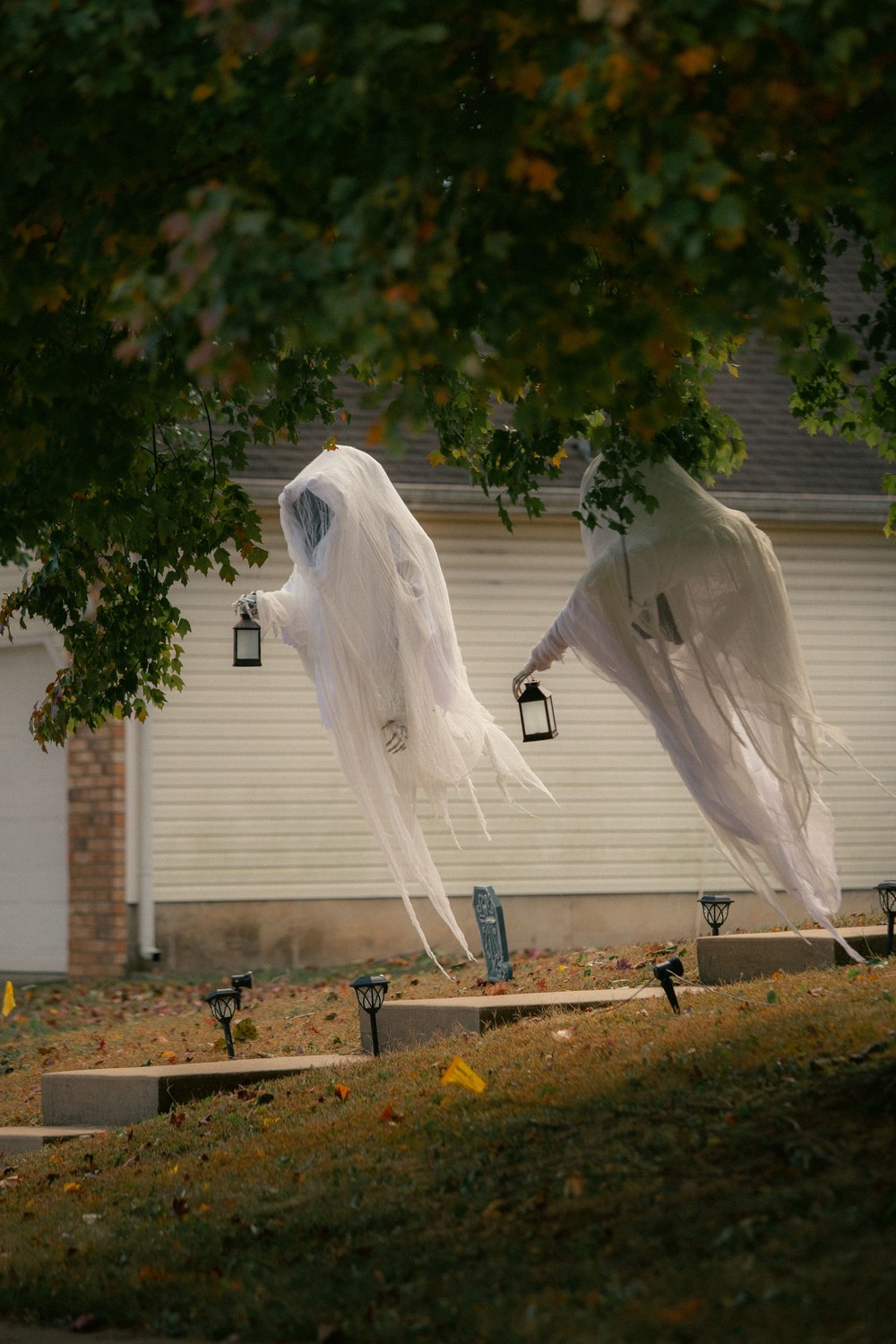 Fantômes en voile blanc suspendus à un arbre dans un jardin avec de petites lanternes
