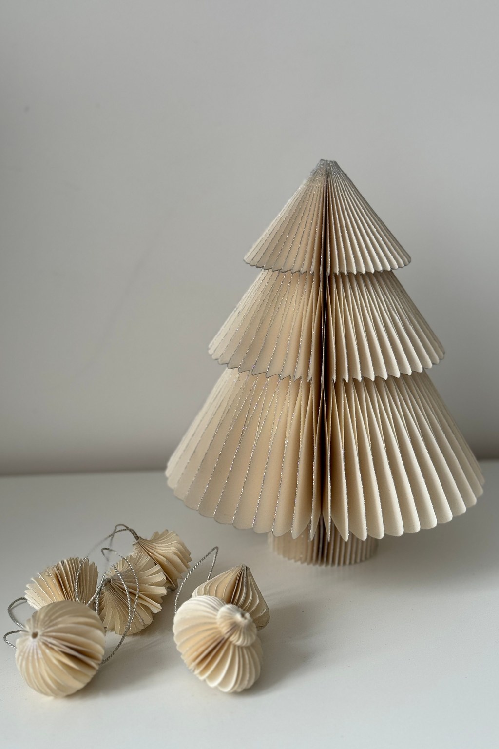 Sapin en papier plissé Sapin en papier plissé de teinte crème posé sur une surface grise près de petites décorations en papier