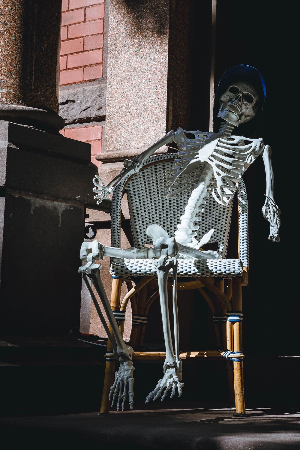 Squelette décoratif assis sur une chaise de terrasse devant une façade en brique